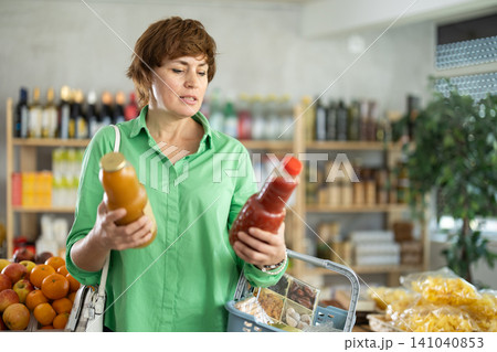 Adult woman chooses peach and tomato juices Adult woman chooses peach and tomato juices 141040853