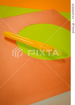 Yellow glue applicator lying on cut orange paper with a circular green paper cutout, ready for crafting, school projects, or hobby activities showcasing creativity and hands on learning Yellow glue applicator lying on cut orange paper with a circular green paper cutout, ready for crafting, school projects, or hobby activities showcasing creativity and hands on learning 141040934