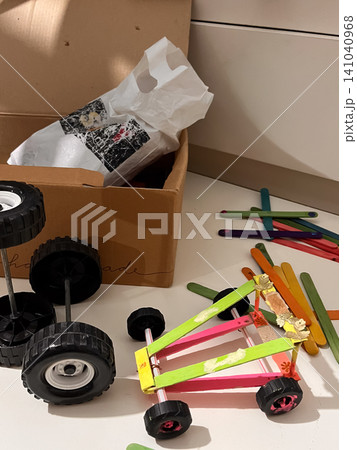 Children engaging in hands on learning, building a small toy car from craft sticks, straws, and plastic wheels, fostering creativity and problem solving skills in a STEM education setting 141040968
