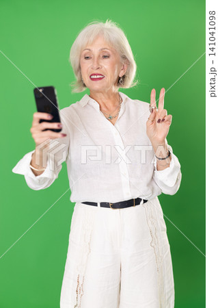 Elderly woman taking selfie in front of green screen Elderly woman taking selfie in front of green screen 141041098