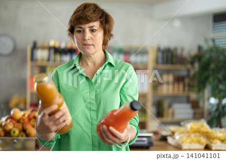 Grocery shopping at supermarket - woman chooses juice, tomato, grapefruit or peach Grocery shopping at supermarket - woman chooses juice, tomato, grapefruit or peach 141041101
