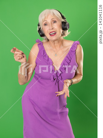 Elderly woman listening to music and dancing in front of green screen Elderly woman listening to music and dancing in front of green screen 141041116