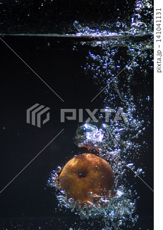 Red apple immersing into clear sparkling water generating a dynamic splash and streams of bubbles Red apple immersing into clear sparkling water generating a dynamic splash and streams of bubbles 141041131