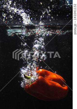 Red bell pepper splashing into fresh clear water creating bubbles Red bell pepper splashing into fresh clear water creating bubbles 141041132