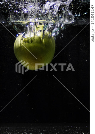 Green apple splashing into clean fresh water creating bubbles .Black background. Copy space 141041147