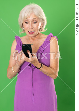 Mature woman in pink dress scrolls phone screen, on green screen background Mature woman in pink dress scrolls phone screen, on green screen background 141041201