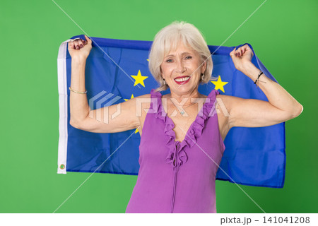 Mature woman in summer clothes with large flag of European Union posing on a green background. Chroma key compositing 141041208