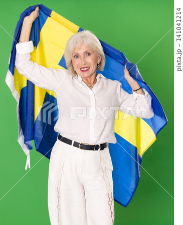 Elderly woman in white clothes with large flag of Sweden posing on green background. Chroma key compositing 141041214