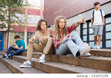 Girl points her hand at someone on the street to guy during break in college Girl points her hand at someone on the street to guy during break in college 141041399