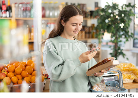 European teen girl customer at shop scans QR code on nougat package using phone camera European teen girl customer at shop scans QR code on nougat package using phone camera 141041408