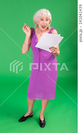 Mature woman in pink dress takes notes in notebook on a green background. Chroma key compositing 141041439