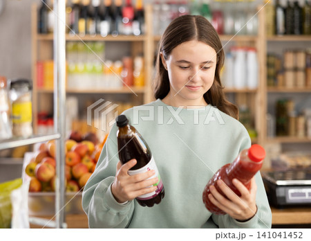 Teen girl hold packages bottles and choose consider juice in store Teen girl hold packages bottles and choose consider juice in store 141041452