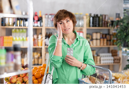 Customer with basket of groceries in hands suffers from headache, feels pain in temple area Customer with basket of groceries in hands suffers from headache, feels pain in temple area 141041453