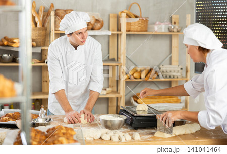 In kitchen employee knead dough, assistant weighs dough piece on scale 141041464