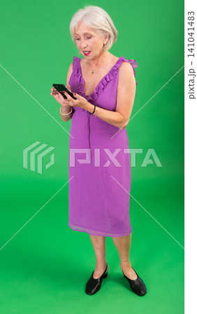 Mature woman in pink dress scrolling through smartphone screen against a green screen background. Chroma key compositing Mature woman in pink dress scrolling through smartphone screen against a green screen background. Chroma key compositing 141041483