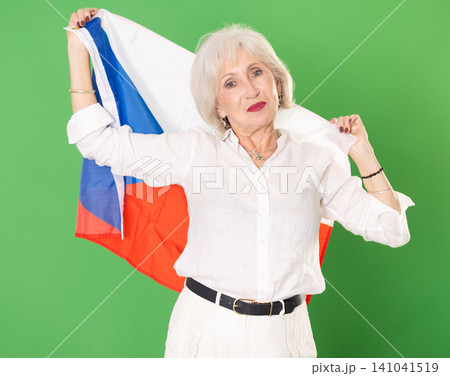 Elderly woman in white clothes with large flag of Czech posing on green background. Chroma key compositing Elderly woman in white clothes with large flag of Czech posing on green background. Chroma key compositing 141041519