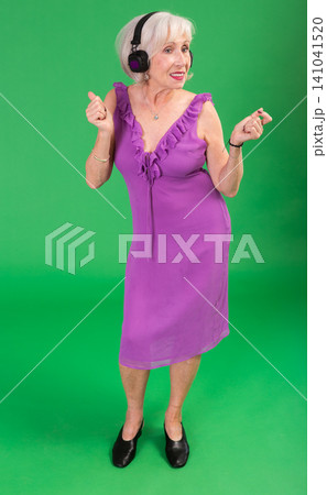 Elderly woman listening to music and dancing in front of green screen Elderly woman listening to music and dancing in front of green screen 141041520