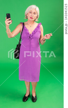 Elderly woman in pink dress takes selfie on a green background. Chroma key compositing. 141041523