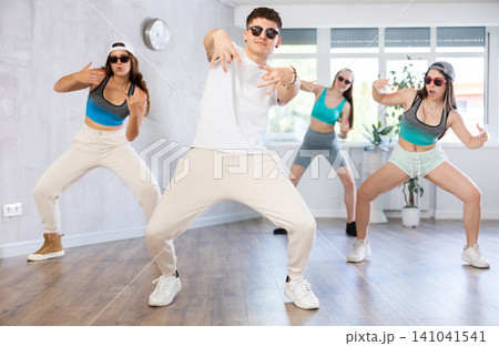 Group of young women and young guy in sunglasses dancing hip hop Group of young women and young guy in sunglasses dancing hip hop 141041541