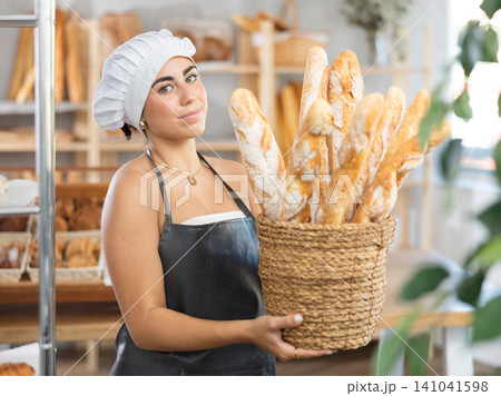 Young female seller with baguettes in basket Young female seller with baguettes in basket 141041598