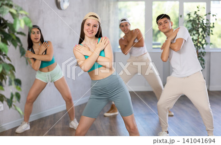 Ordinary teen girls and boy performing kick step movement during training together in dance studio 141041694