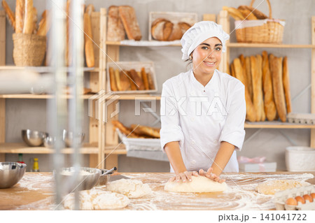 Young woman baker kneads the dough in bakery 141041722