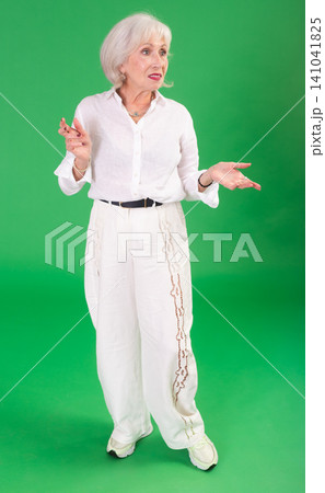 Elderly woman in white clothes looks and looks around on green background Elderly woman in white clothes looks and looks around on green background 141041825