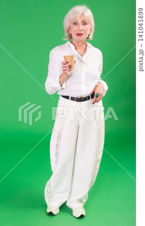 Elderly woman drinking coffee in front of green screen Elderly woman drinking coffee in front of green screen 141041899