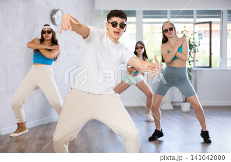 Guy and group of young girls in dark glasses and ball cap dance modern Jazz-modern in fitness club 141042009
