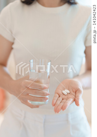 woman hand holding medicine painkiller pill and water glass on the sofa at home, taking for headaches, stomach ache, Diarrhea Pain from food poisoning, Endometriosis, Hysterectomy and Menstrual 141042423