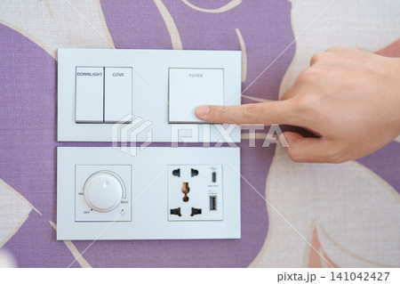finger pushing for turn on light switch on white wall at home room. Woman hand turn off lighting Switch. Energy Saving, energy power control, electrical, eco environment, and lifestyle concept finger pushing for turn on light switch on white wall at home room. Woman hand turn off lighting Switch. Energy Saving, energy power control, electrical, eco environment, and lifestyle concept 141042427