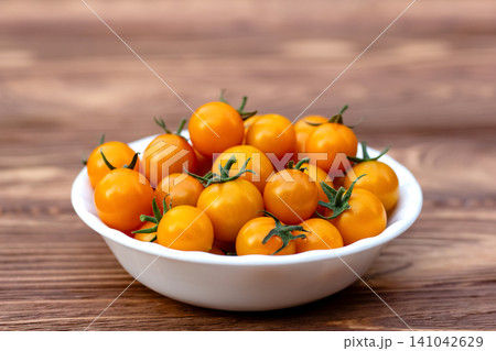 Orange cherry tomatoes in a bowl on the wooden table in the garden. Orange cherry tomatoes in a bowl on the wooden table in the garden. 141042629