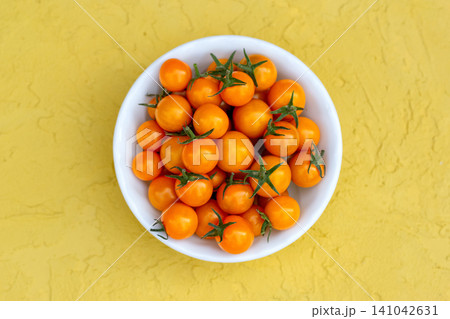 Vivid orange cherry tomatoes in a bowl on the yellow table. Vivid orange cherry tomatoes in a bowl on the yellow table. 141042631