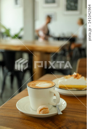 A cup of coffee sits on a table with a dessert nearby A cup of coffee sits on a table with a dessert nearby 141042964