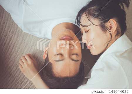 ラグの上で目を閉じ寄り添いながら眠る二人の睡眠美容イメージ俯瞰カップルポートレート ラグの上で目を閉じ寄り添いながら眠る二人の睡眠美容イメージ俯瞰カップルポートレート 141044022
