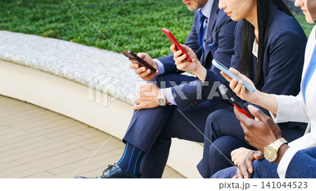 屋外ベンチでスマホを見る多国籍ビジネスパーソンのグループ 141044523