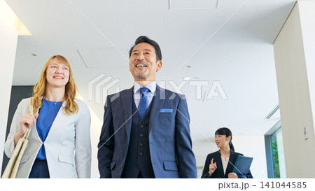 ビルの中を歩きながら会話する多国籍ビジネスパーソンのグループ ビルの中を歩きながら会話する多国籍ビジネスパーソンのグループ 141044585