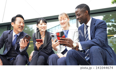屋外ベンチでスマホを見る多国籍ビジネスパーソンのグループ 屋外ベンチでスマホを見る多国籍ビジネスパーソンのグループ 141044674