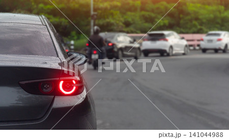 Rear view of sedan car with turn on brake light. Car was wet from the rain. Cars and motorcycles were parked in a line along the curve in the road, waiting to pass by. with green forest background. Rear view of sedan car with turn on brake light. Car was wet from the rain. Cars and motorcycles were parked in a line along the curve in the road, waiting to pass by. with green forest background. 141044988