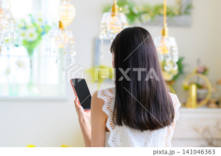 室内でスマートフォンを持つ女性の後ろ姿 室内でスマートフォンを持つ女性の後ろ姿 141046363