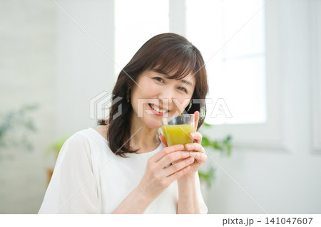 リビングで野菜ジュースを飲む60代の女性 リビングで野菜ジュースを飲む60代の女性 141047607