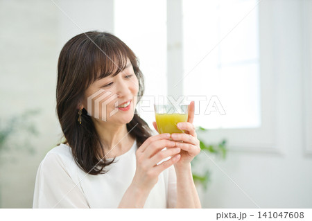 リビングで野菜ジュースを飲む60代の女性 リビングで野菜ジュースを飲む60代の女性 141047608