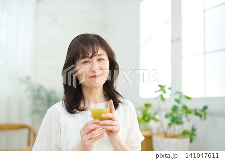 リビングで野菜ジュースを飲む60代の女性 リビングで野菜ジュースを飲む60代の女性 141047611