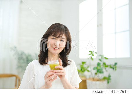 リビングで野菜ジュースを飲む60代の女性 リビングで野菜ジュースを飲む60代の女性 141047612