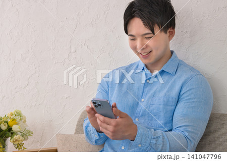 スマホを見ながらソファでくつろぐ若い男性 141047796