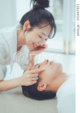 仰向けに横たわる彼氏の頬に触れながら大きく笑う彼女のカップル美容イメージ縦位置ポートレート 141047951