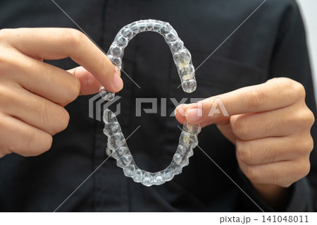 Man holding invisible aligner orthodontic retainer for dental teeth straightening. Man holding invisible aligner orthodontic retainer for dental teeth straightening. 141048011