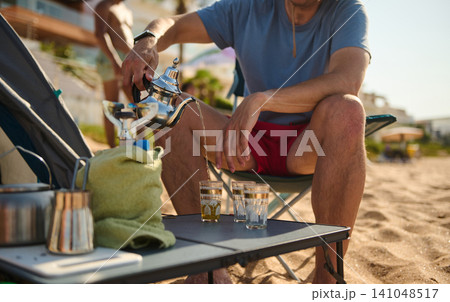 Man pouring tea on a sandy beach during a relaxed summer vacation 141048517
