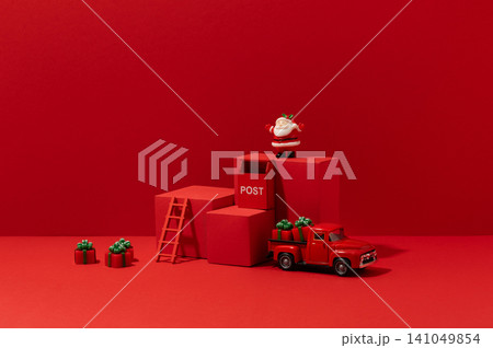 Bright Christmas product display scene with vintage toy truck, podium props, and holiday decorations against a bold monochromatic red studio background. 141049854