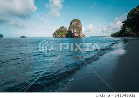 Beautiful view of a limestone karst island from a sandy beach under an overhanging cliff in Krabi, Thailand. Beautiful view of a limestone karst island from a sandy beach under an overhanging cliff in Krabi, Thailand. 141049932